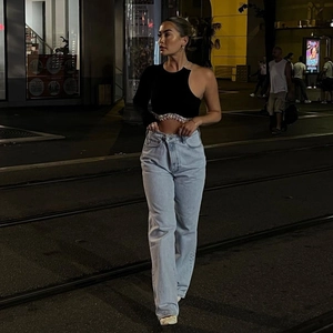 Détail du top noir asymétrique à franges argentées et jean bleu clair à taille haute