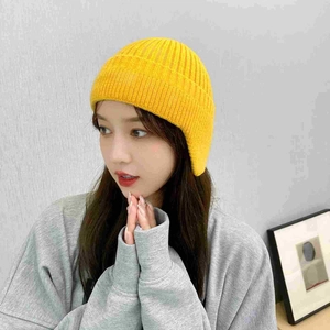 Detail view of a cozy yellow knitted winter earflap hat worn by a model in casual style