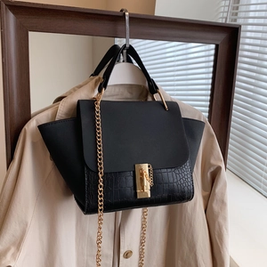 Detail of black trapezoid bag with crocodile pattern and golden chain on trench coat