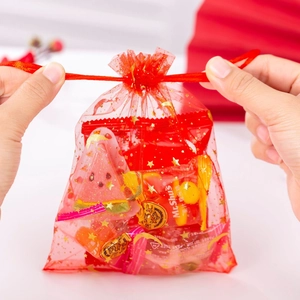 Close-up of red organza bag with gold stars being closed by drawstring with candies