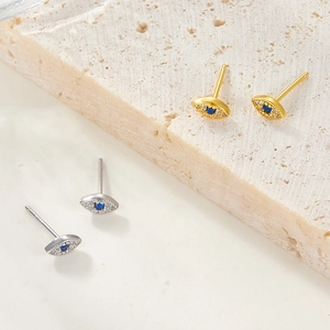 Macro detail of gold and silver Evil Eye earrings featuring blue zircon inlays on stone