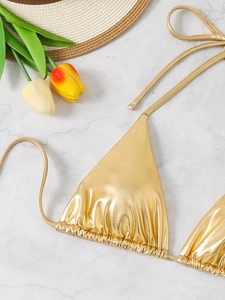 Detail view of a sexy gold metallic bikini top with halter neck straps on marble background