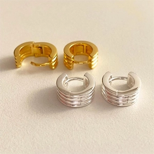 Macro shot of minimalist gold and silver ribbed C-shape earrings on cream background