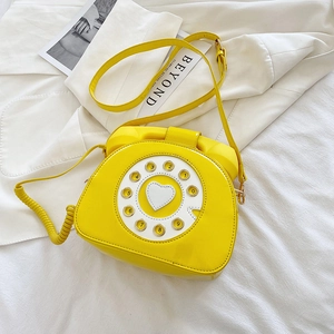 Detail of yellow retro telephone purse with spiral handle and heart dial on white background