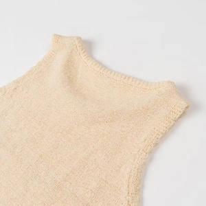 Dettaglio del gilet in maglia beige con trama intrecciata su colletto e spalle su bianco