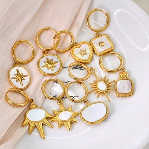 Flat lay of gold earrings with white shell charms on white ceramic tray with pink silk
