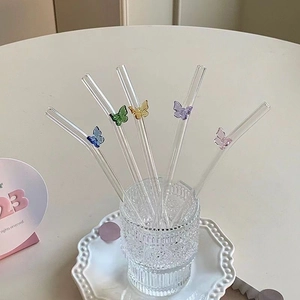 Close-up of five colored glass straws with butterfly decorations in a textured glass cup