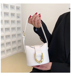 Detail view of mini white leather bucket bag with large gold U-buckle on a female model