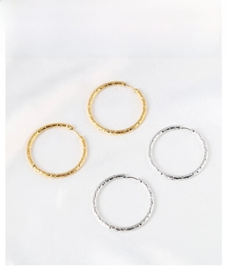 Detailed view of hammered gold and silver hoop earrings on elegant white silk fabric