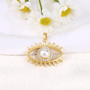 Detailed view of gold-plated evil eye pendant with pearl and rhinestones on white ceramic