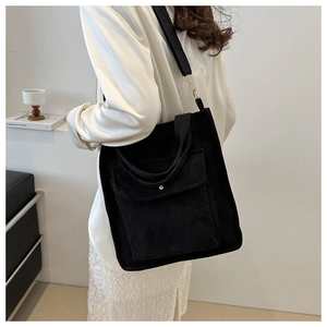 Detail of black corduroy tote bag showing front pocket texture and adjustable strap