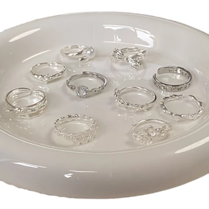 Collection of silver 925 rings with pearl, floral, and bow designs on white plate