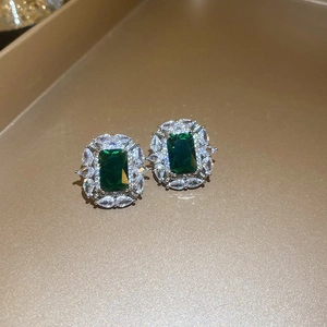 Dettaglio macro di orecchini a lobo con zircone verde taglio smeraldo su vassoio oro