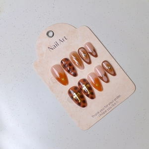 Detail of almond press-on nails with leopard print, orange gradient and golden cross charms