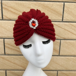 Detail of burgundy knitted turban hat featuring a large red gemstone and pleated texture