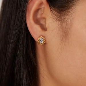 Gold flower earrings with oval cubic zirconia centerpiece shown on a model