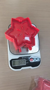 Weight measurement of a red star-shaped 3D Christmas tree cookie mold on a kitchen scale