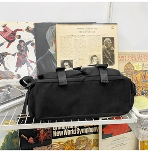 Detail of black canvas messenger bag with double buckles against a vintage record wall