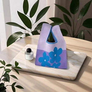 Dettaglio di borsa regalo in maglia viola con fiori blu su vassoio di marmo