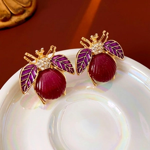 Macro detail of vintage beetle stud earrings with purple enamel and sparkling crystals