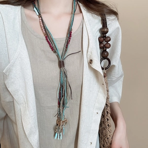 Detail of bohemian multilayer necklace with colorful beads and fringes on linen clothing