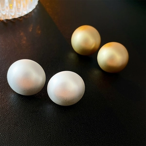 Minimalist matte gold and pearl sphere earrings displayed on black textured background