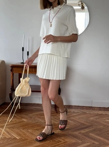 Draußen-Aufnahme von Creme-Polo-Top und Faltenrock-Set mit gelber Tasche und braunen Sandalen