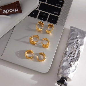 Drei Paar elegante 18k vergoldete Herz- und Blumenohrringe auf einer Laptop-Oberfläche