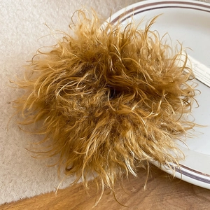Detailed view of a brown plush hair tie with soft faux feather texture on a white plate