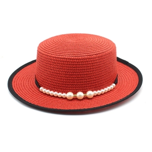 Close-up of red straw hat with black edge trim and elegant pearl bead decoration