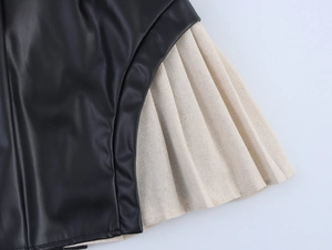 Close-up of black PU leather contrast stitching with beige pleated skirt hem detail