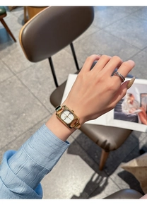 Detail of elegant gold square watch on woman's wrist in a stylish cafe setting