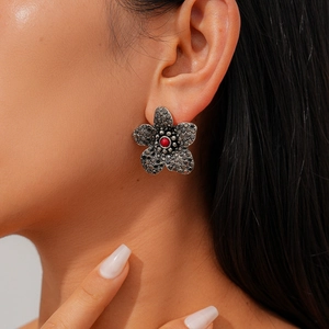 Nahaufnahme eines dunklen Blumenohrsteckers mit roter Perle am Ohr des Models