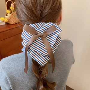 Détail d'un grand nœud en tissu rayé avec des rubans marrons sur cheveux tressés