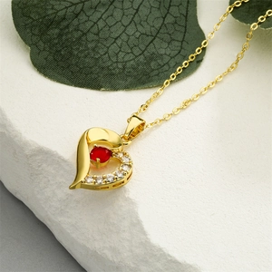 Macro view of gold heart pendant necklace with red gemstone and sparkling zircons
