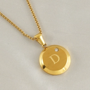 Macro shot of gold pendant necklace with letter D engraving and small zircon diamond