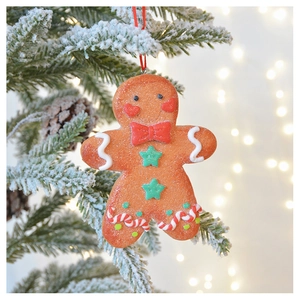 Close-up of a gingerbread man ornament hanging on a snowy Christmas tree with bokeh lights