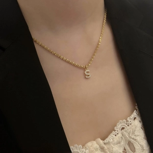 Détail du pendentif lettre S en acier titane doré serti de zircons sur une femme