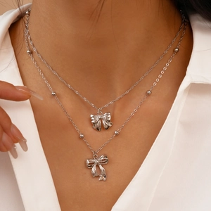 Gros plan d'un collier multicouche argenté avec pendentifs nœuds porté par un mannequin
