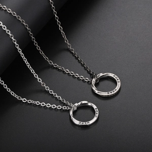 Detail of two silver Mobius ring pendants with ROAD HERE engraving on a dark texture background