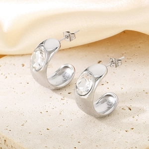 Detail of silver C-shaped earrings with oval clear stones on beige stone and silk
