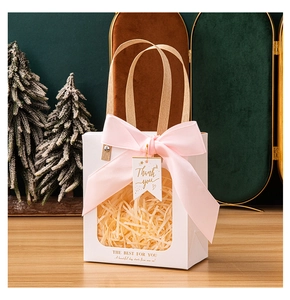 Close-up of elegant white gift bag with transparent window, pink ribbon, and gift tag