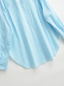 Detailed view of curved hem and stitching on light blue cotton button-up shirt