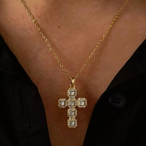 Close-up of gold cross pendant with zircon stones on a black shirt worn by a model