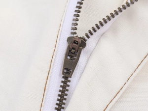 Detail shot of antique bronze metal zipper on high-waist white wide-leg trousers