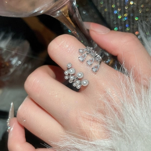 Detailed view of multilayer pearl and zircon open ring worn on finger with fur sleeve
