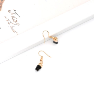 Close-up of raw black stone drop earrings with gold hooks on a minimalist background