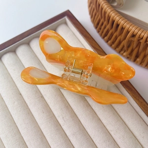Close-up of orange marble acetate claw clip with golden metal spring on beige velvet