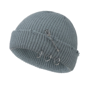 Close-up of greyish blue knitted beanie featuring three metal rings and a large safety pin