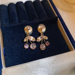 Close-up of cherry earrings with pink and purple zircons on dark velvet background